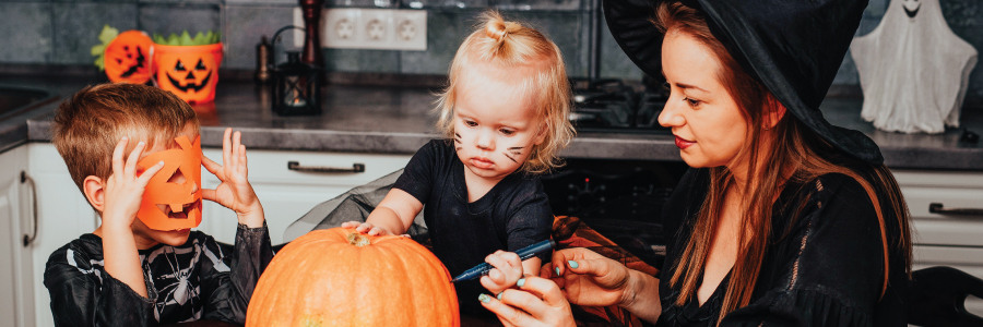 A mother and her two children decorating a pumpkin in their kitchen.