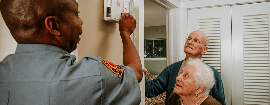 A firefighter showing a fire alarm to older adults in their home.