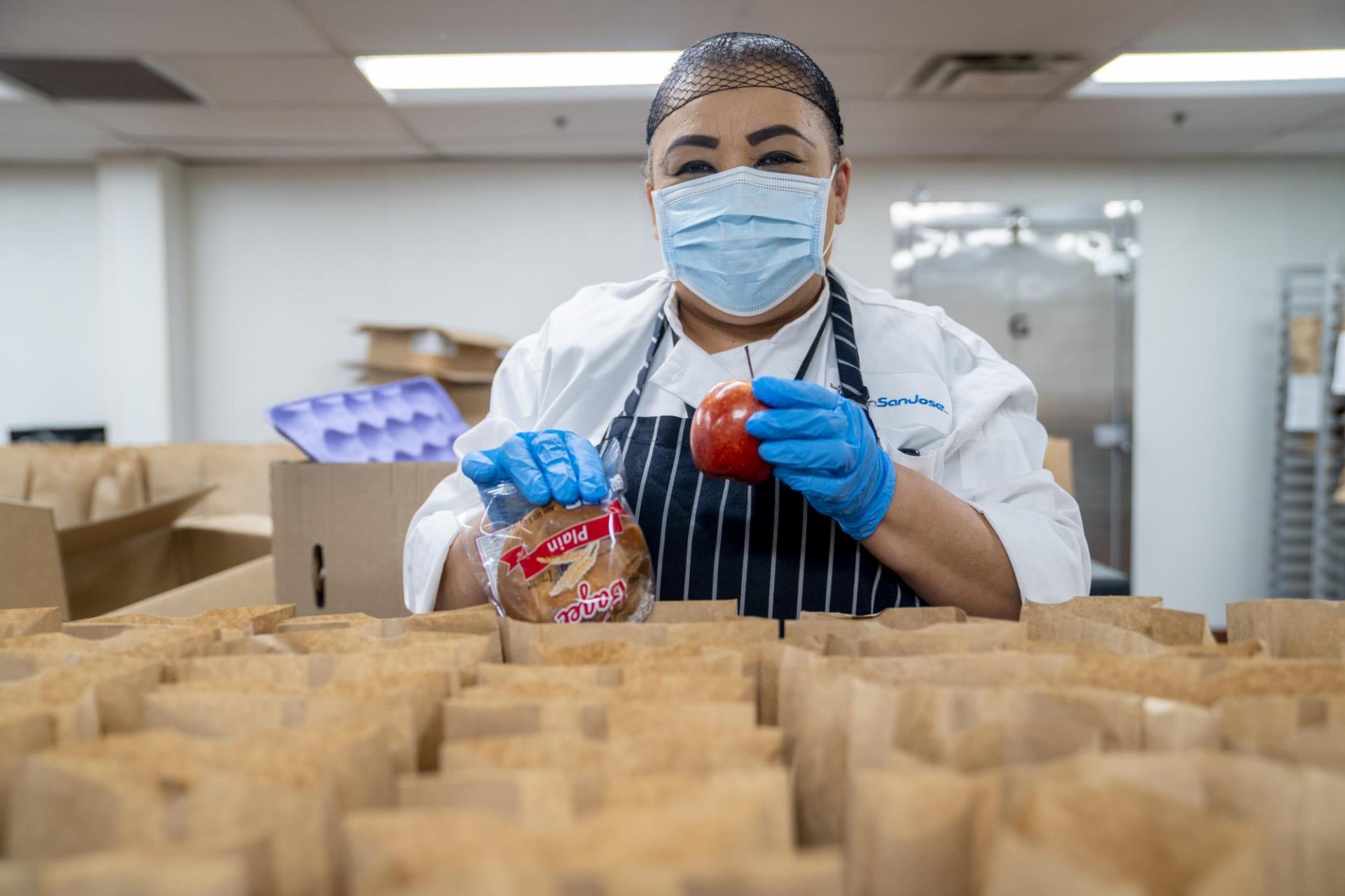 Woman packaging apples to brown paper bags for food distribution