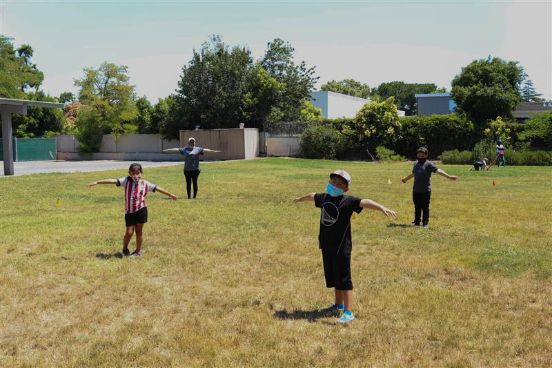 Kids and staff in masks, social distancing in an open grassy area