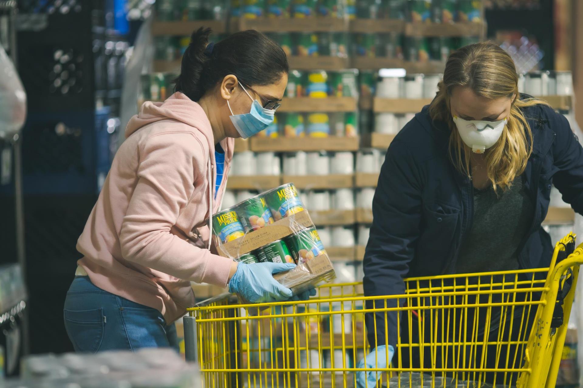 Two people wearing masks loading pre packaged goods for food distribution