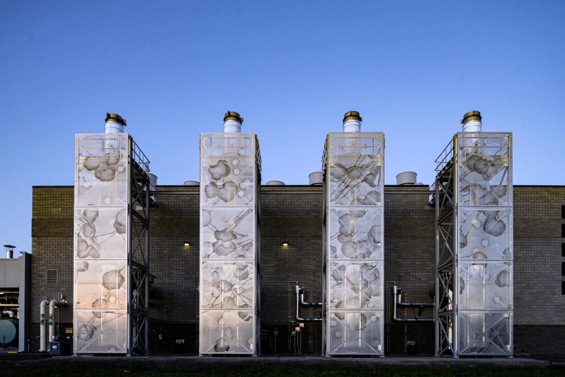 Four stainless steel screens installed on the façade of the Cogeneration Plant at dawn.