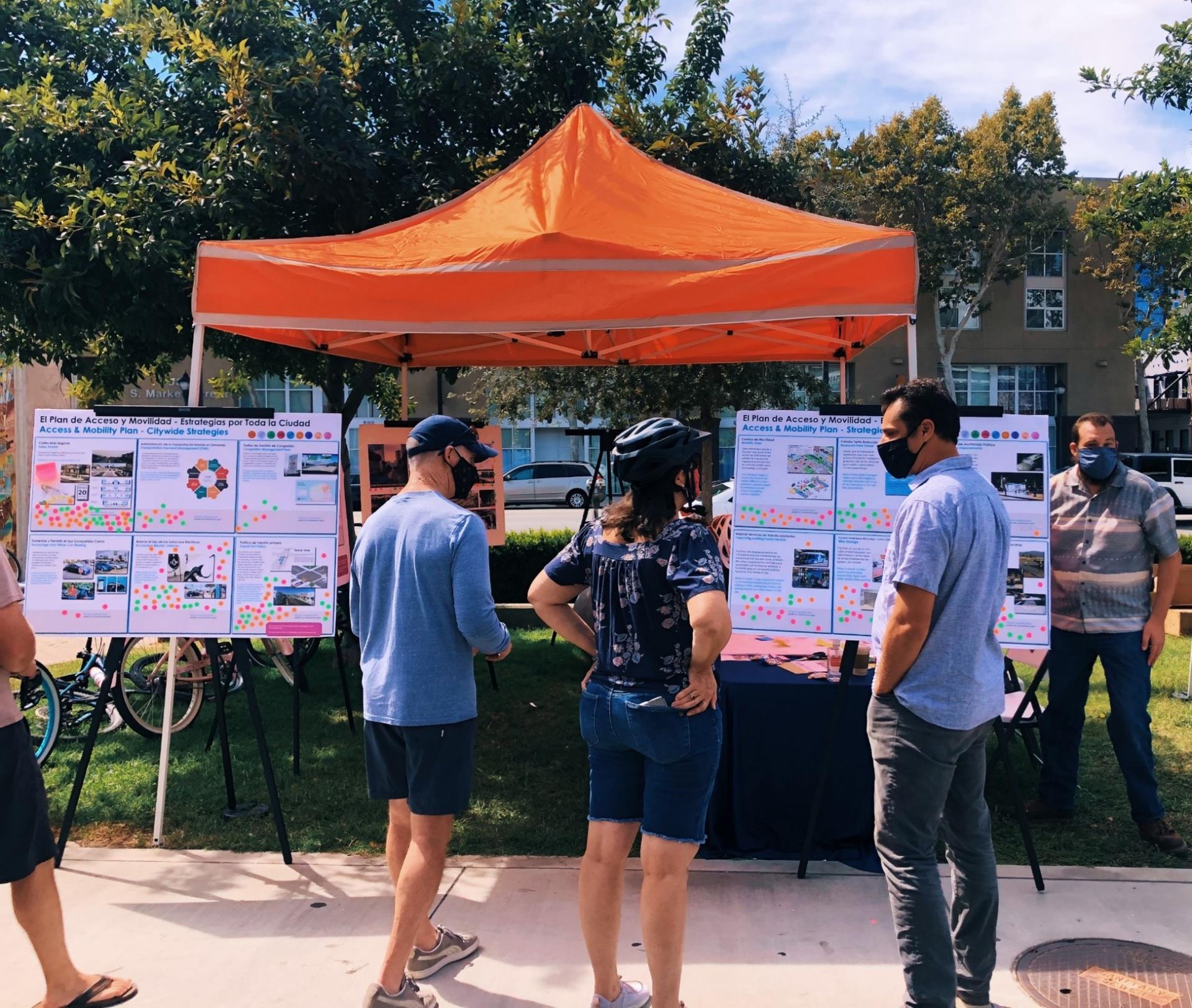 Image of three masked people standing at an outreach booth in front of presentation boards covered in images and stickers