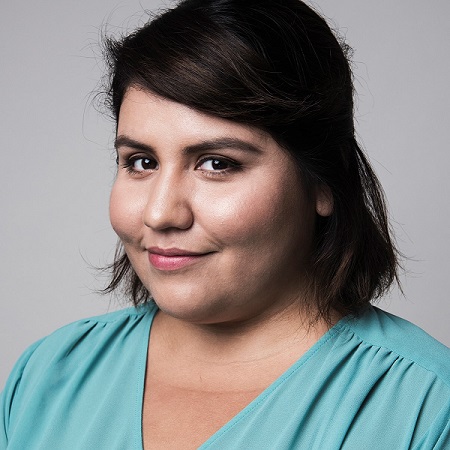 Woman with olive complexion, wearing an aqua colored blouse with a V-neck, shoulder-length dark brown hair with swoop bangs.