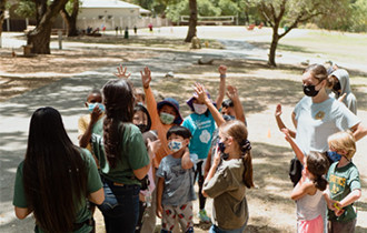 PRNS Summer Camp Outside with Kids Raising Hands