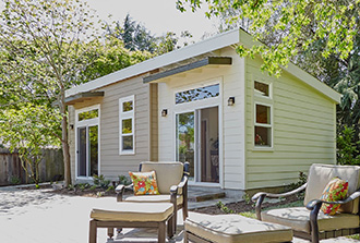 A pastel painted additional dwelling unit with white trimmed windows on a sunny day