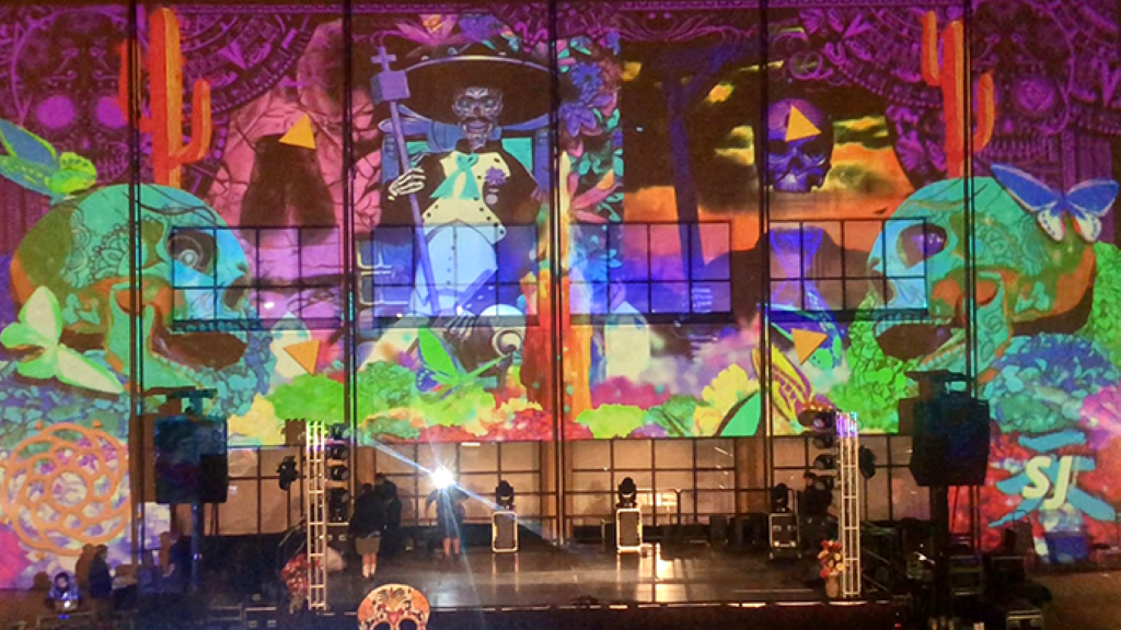 Projected video wall of colorful skulls and a magical universe. Projected on top of a stage.