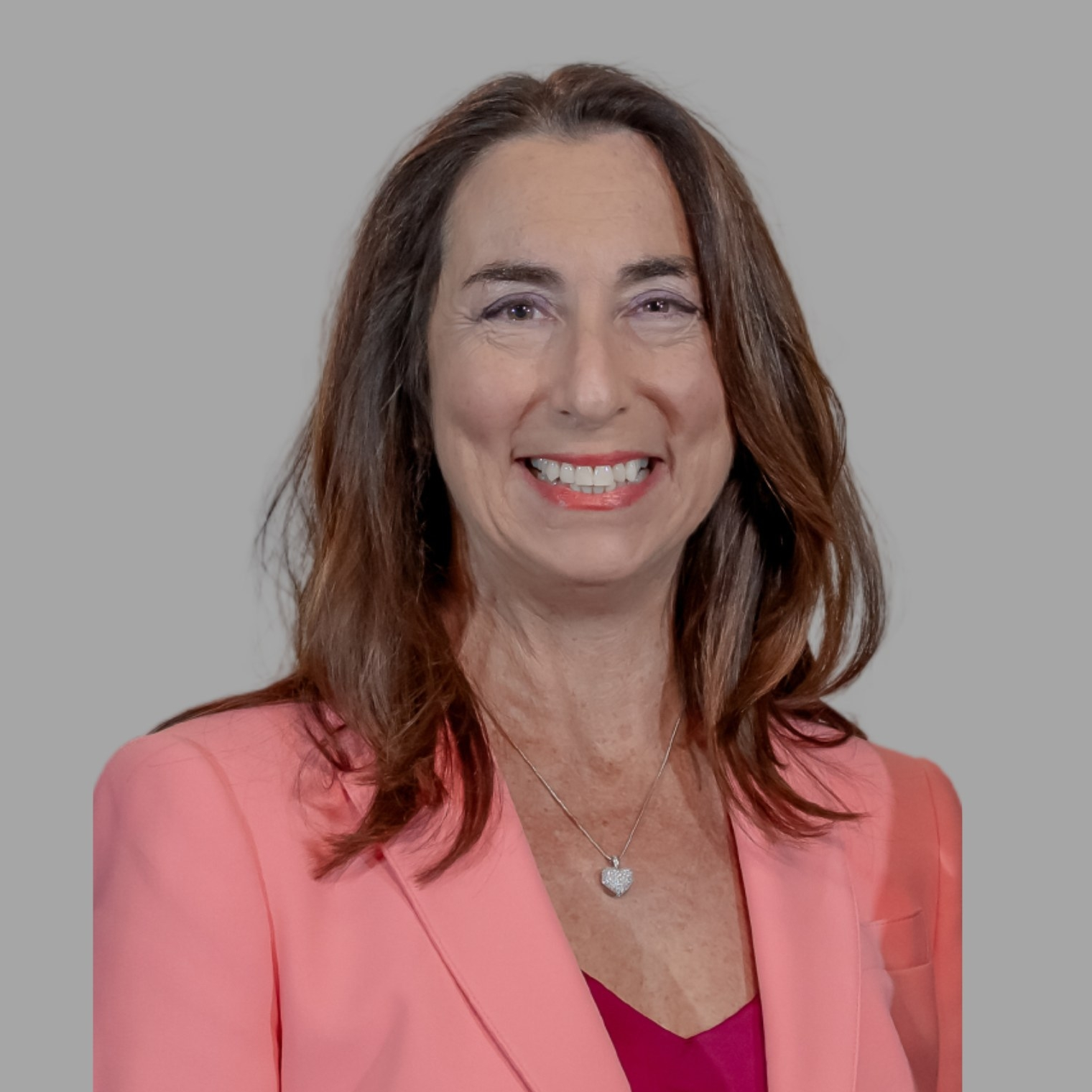 Susan Ellenberg, a woman smiling with long brown hair wearing a pink blazer in front of a plain white background.