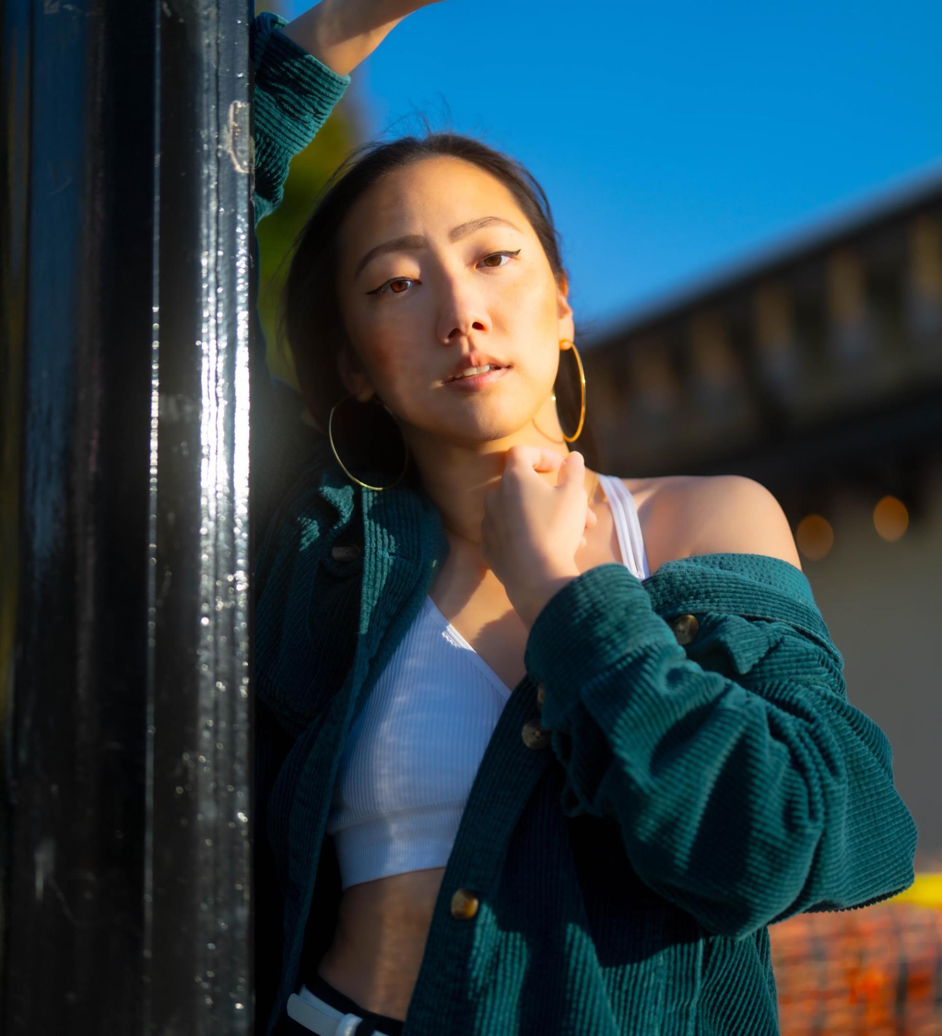 Portrait of an Asian woman in her late 20's - early 30's weearing gold hoop hearings. Her hands are under her chin with arms and elbow down in a v-shape.