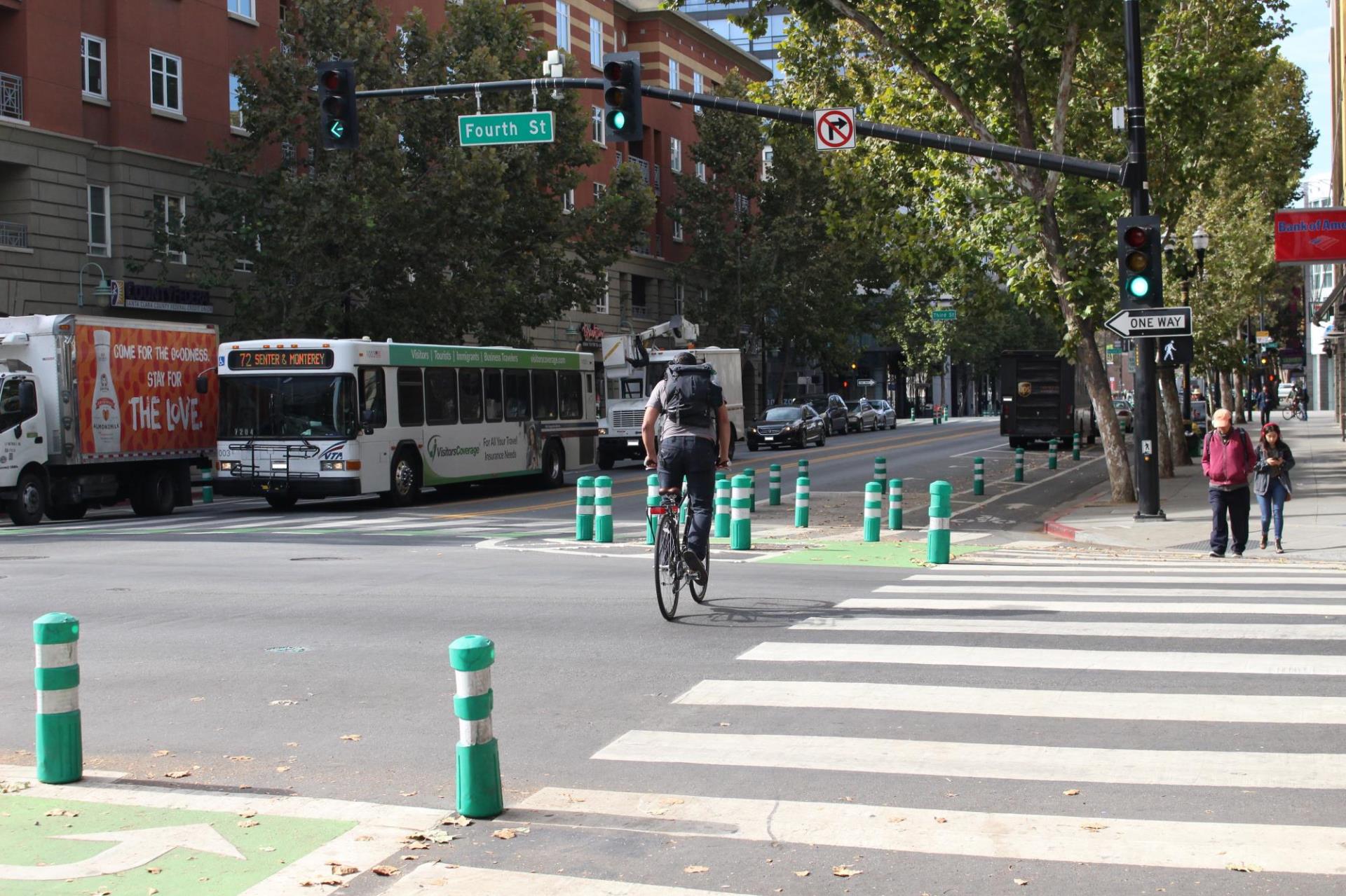 A bike rider biking in a protected bike lane, surrounded by green, flexible bollards, on Fourth Street and San Fernando Street