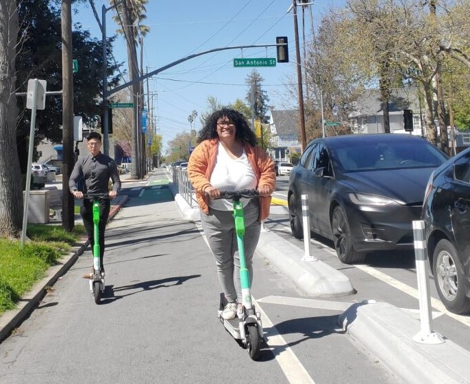 Two people riding electric scooters in a protected bike lane