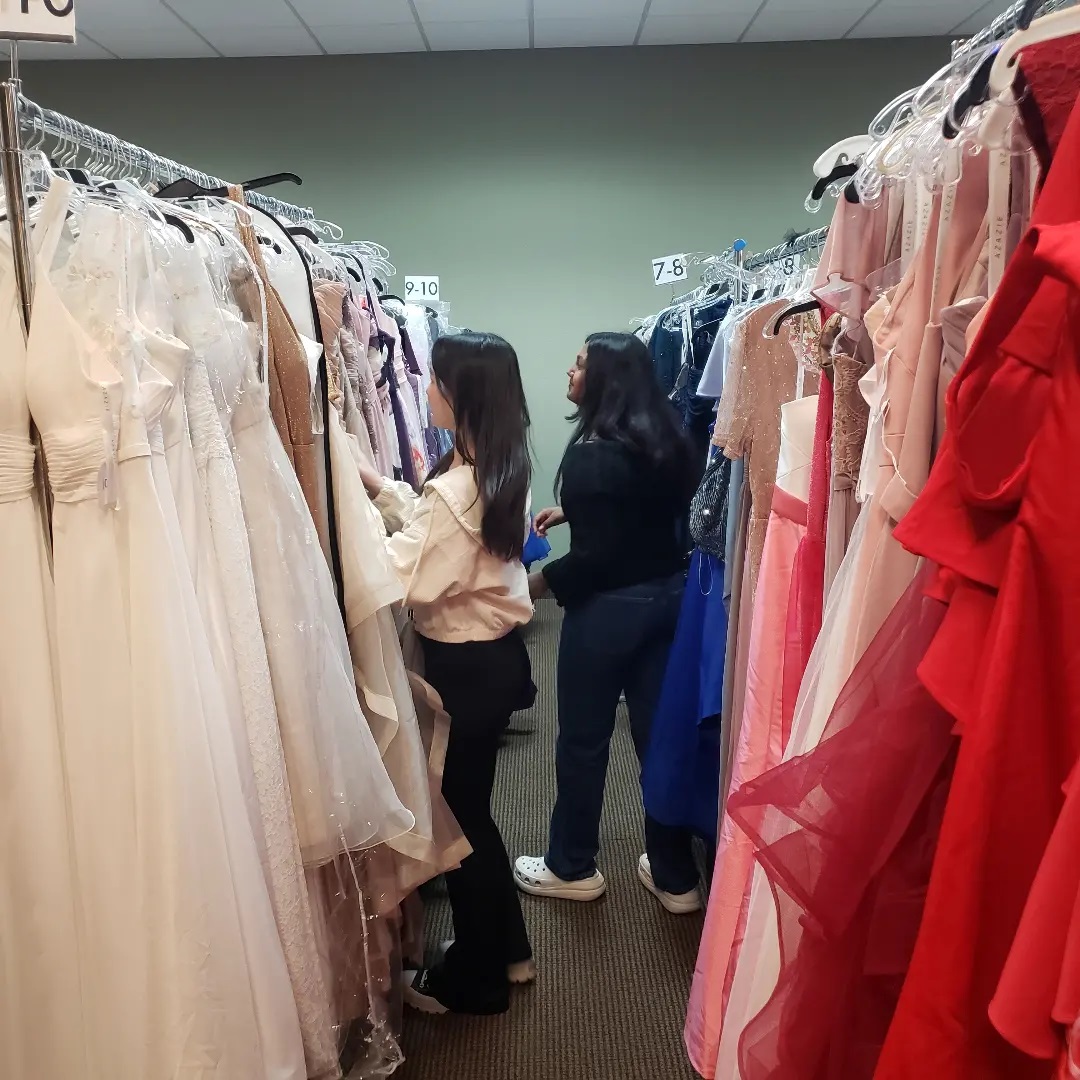 Two youth participants look through racks of beautiful prom dresses.