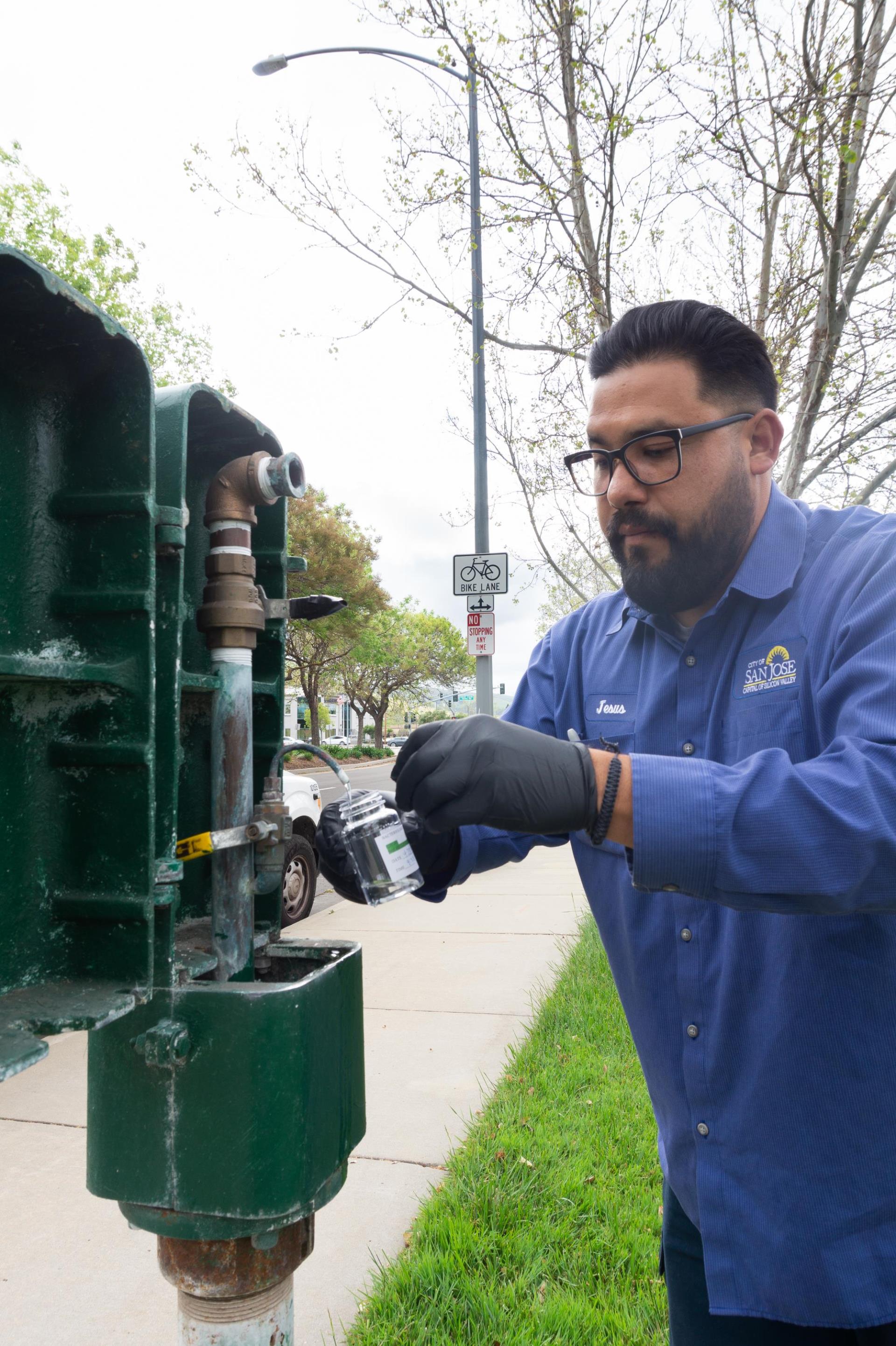 A man with glasses in a blue collared shirt collecting a weekly water sample to ensure customers receive safe drinking water