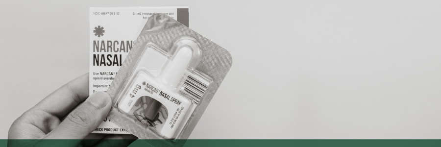 A hand holding a NARCAN spray and box.