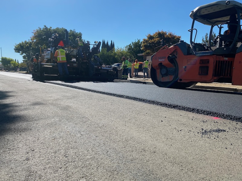 paving machines roll out a stripe of asphalt on a street