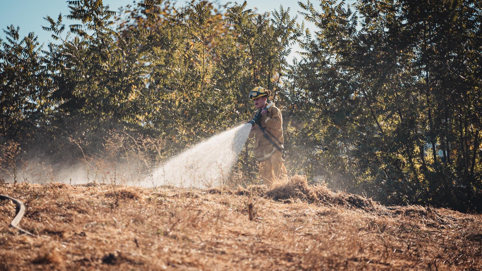 An SJFD firefighter extinguishes burning grass with a hose