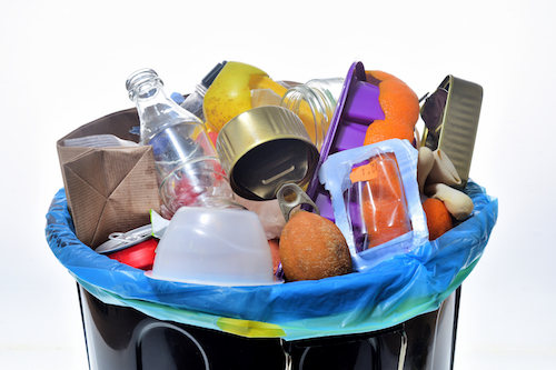 A trash can topped with a mixed collection of trash, from plastic bottles to food scraps